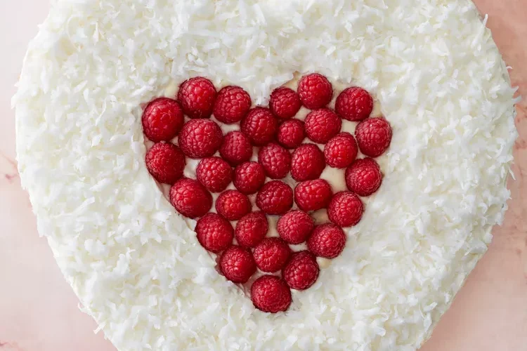 Серцеподібний торт, прикрашений білими кокосовими стружками та меншим серцем із червоних малин.
