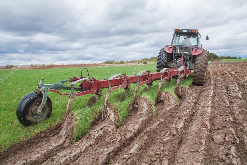 Трактор с плугом выполняет глубокую вспашку поля